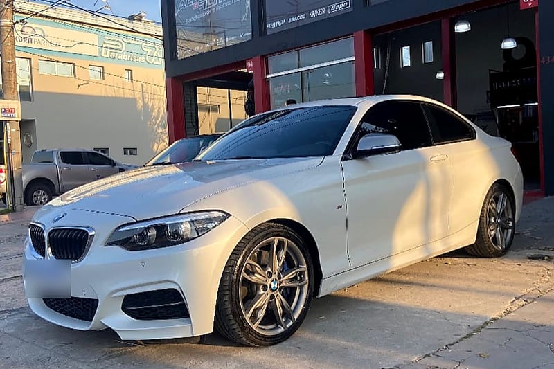 Un BMW Serie 2 blanco estacionado en la puerta del taller, bajo los carteles de reprogramación de ECU y accesorios.