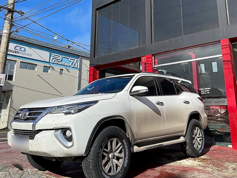 Una Toyota SW4 blanca estacionada en la puerta del taller, con la fachada gris y roja detrás.
